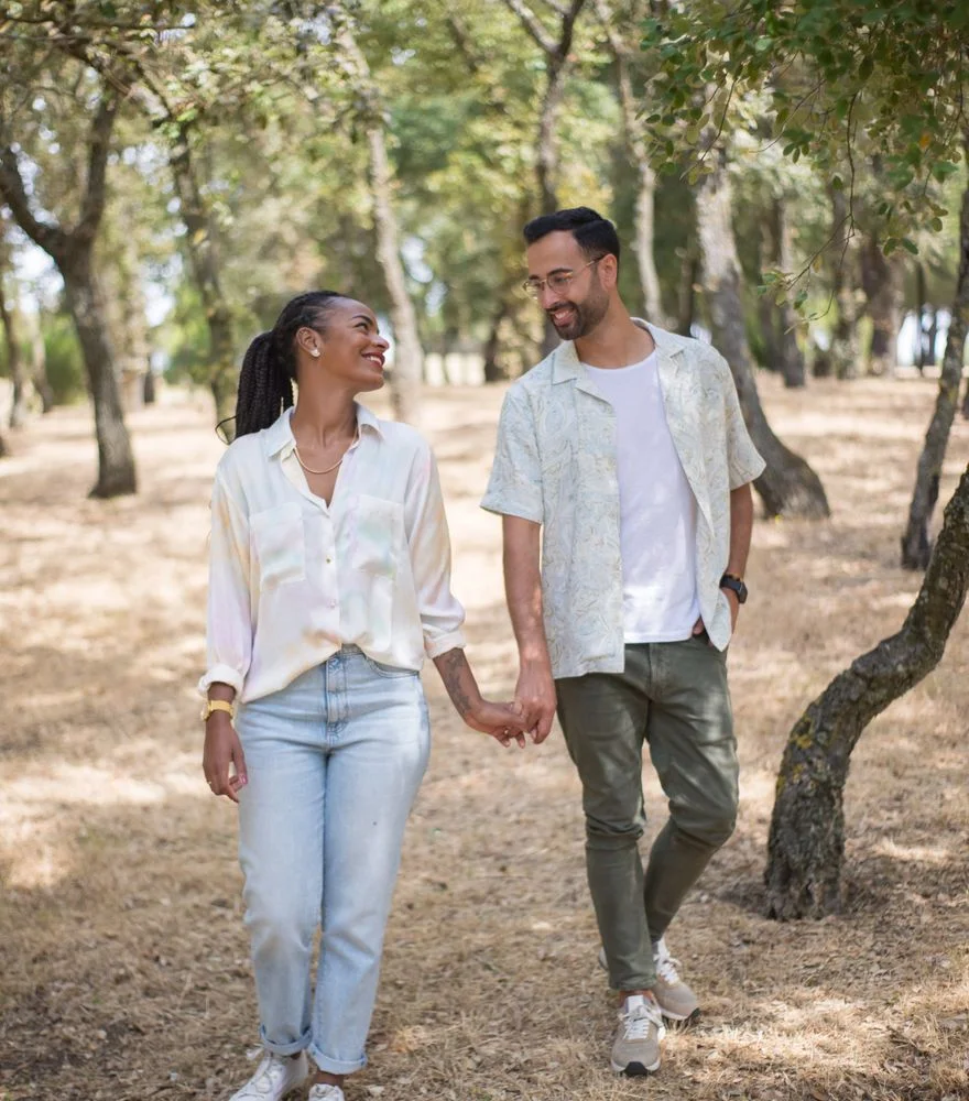 A smiling man and woman walking hand in hand through a sunlit park